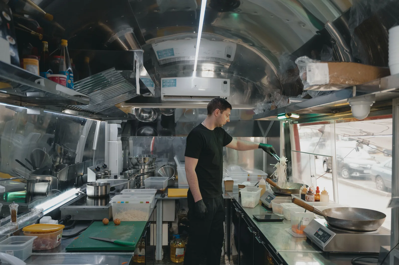 A cook working alone at the range inside the stainless steel galley of a food truck