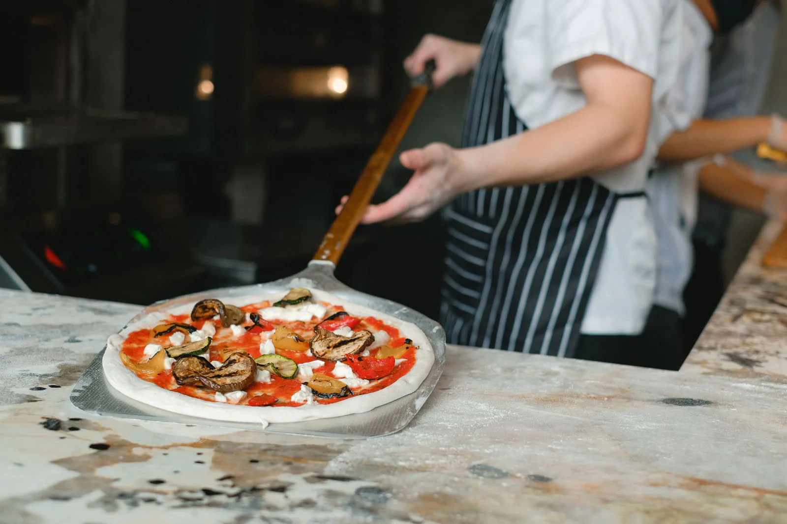A cook sliding a topped pizza into the oven on a peel