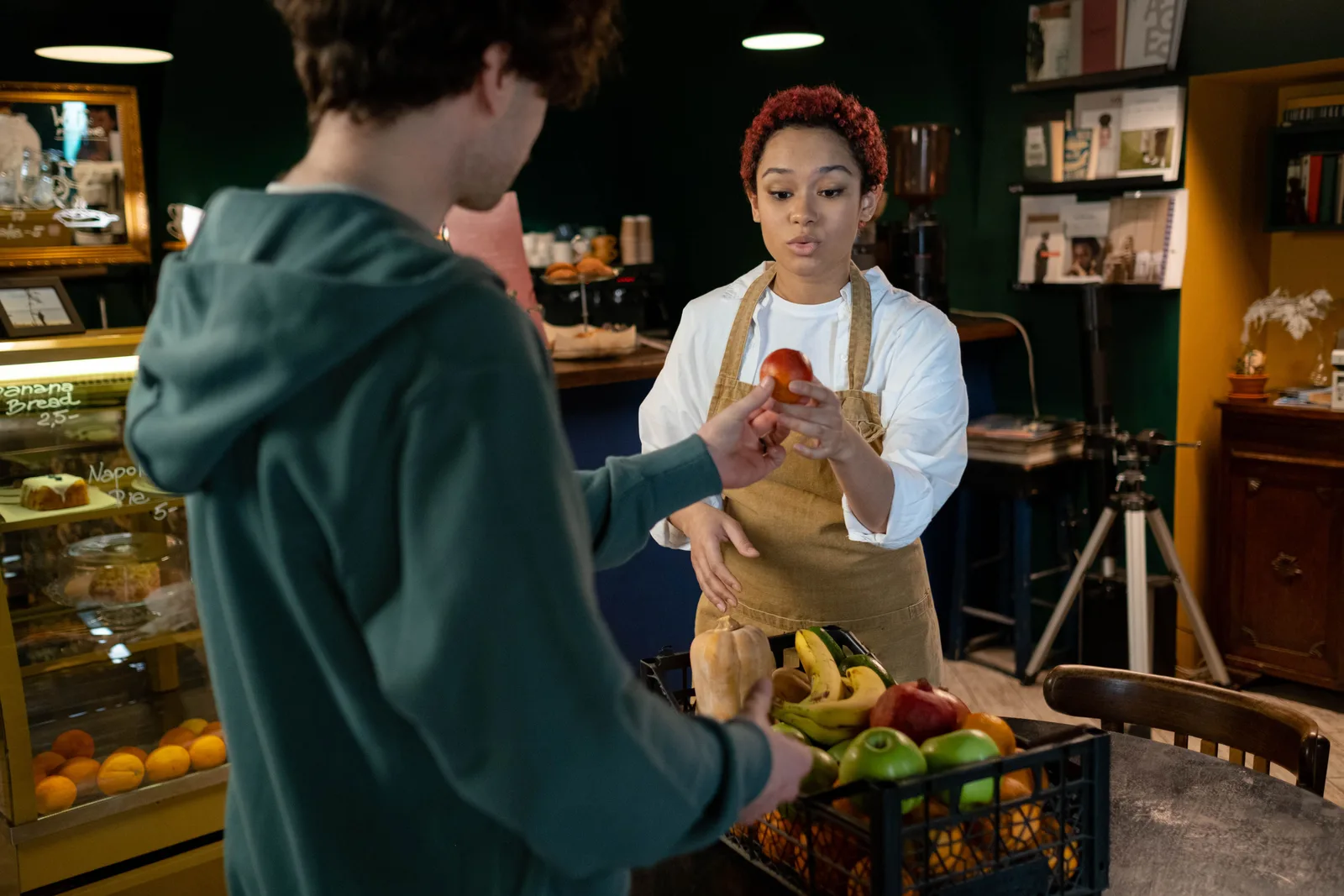 Shop assistant in an apron handing produce to a customer across a service counter