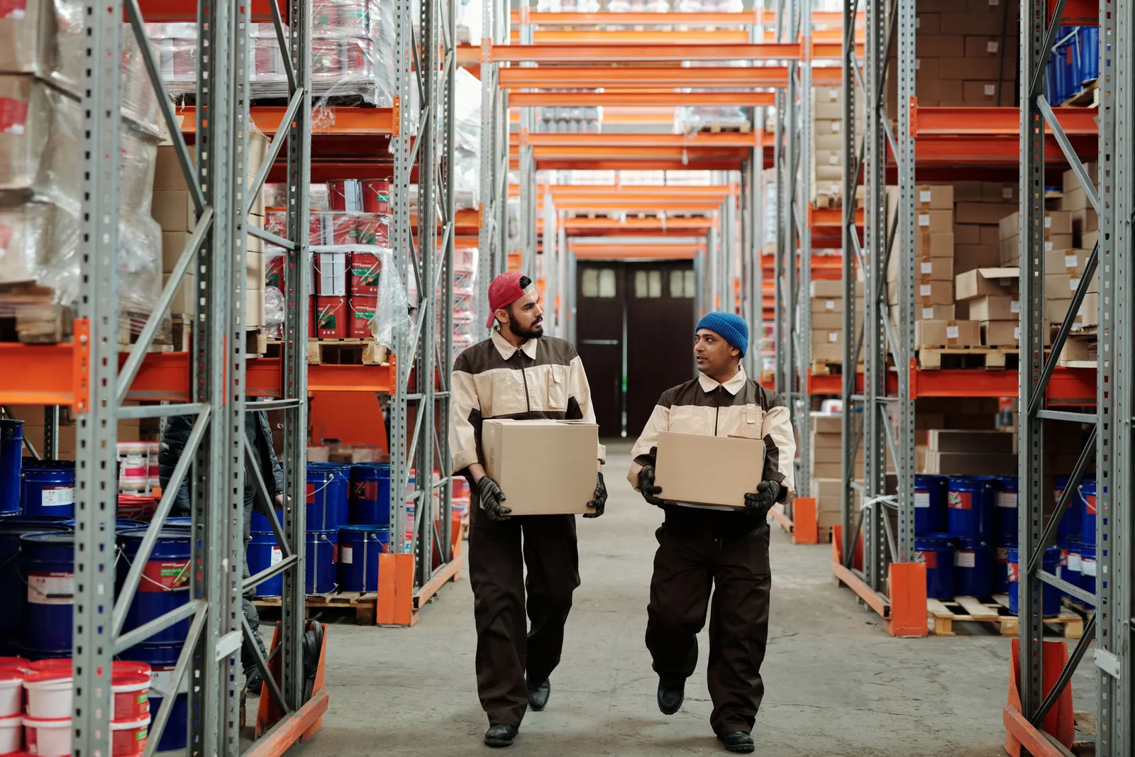 Two workers carrying boxes down a stocked warehouse aisle