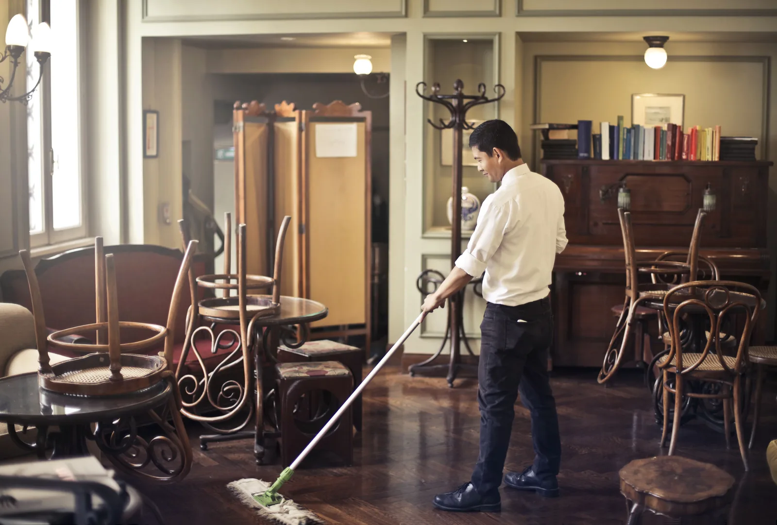 A worker mopping the floor of a hospitality dining room with the chairs stacked on the tables.