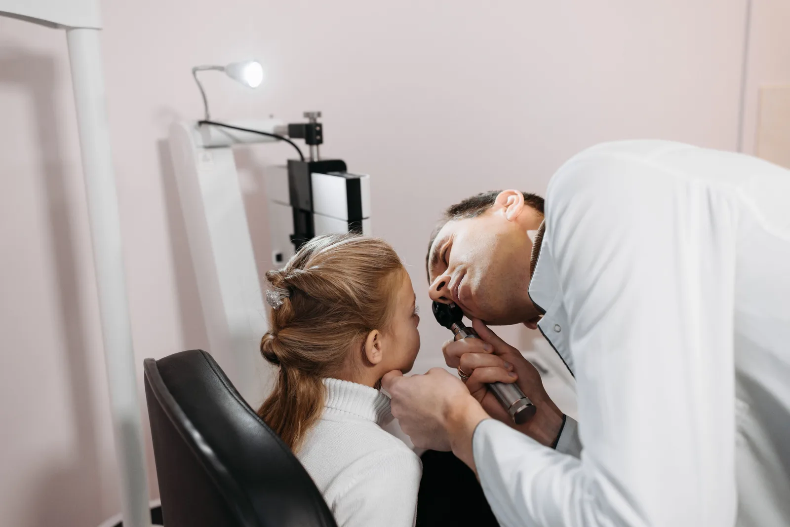 A clinician examining a young child's ear with a hand-held instrument during an appointment
