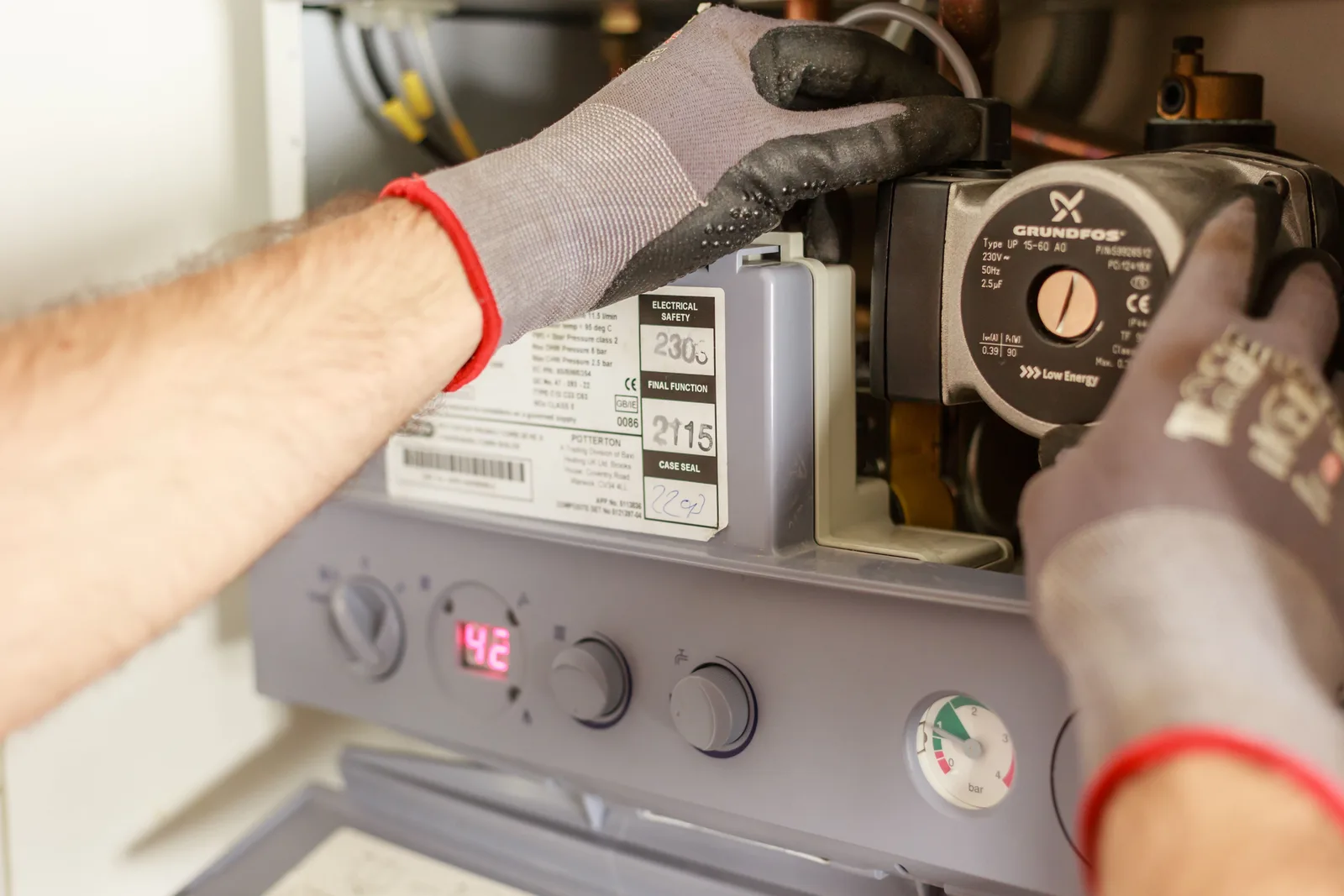 Gloved hands adjusting the controls on a wall mounted water heating unit