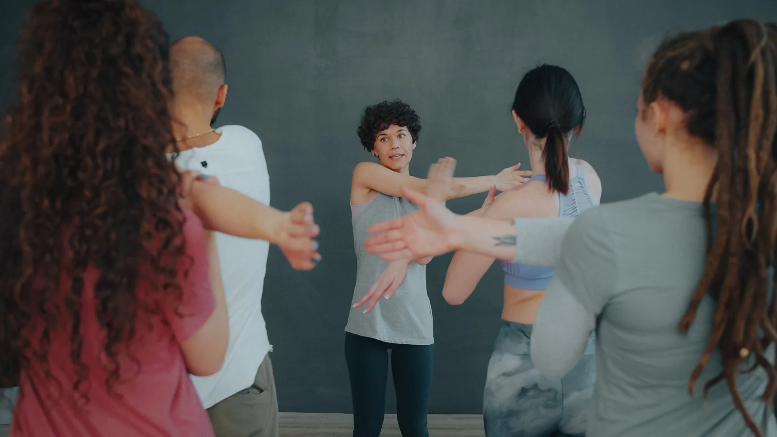 An instructor leading a group fitness class through a stretch in a studio