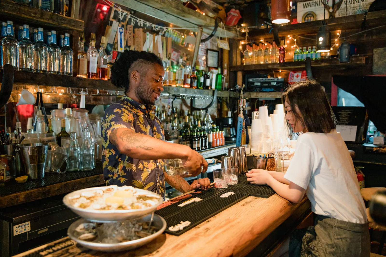 A bartender pours a drink for a customer across the counter of a small independent bar