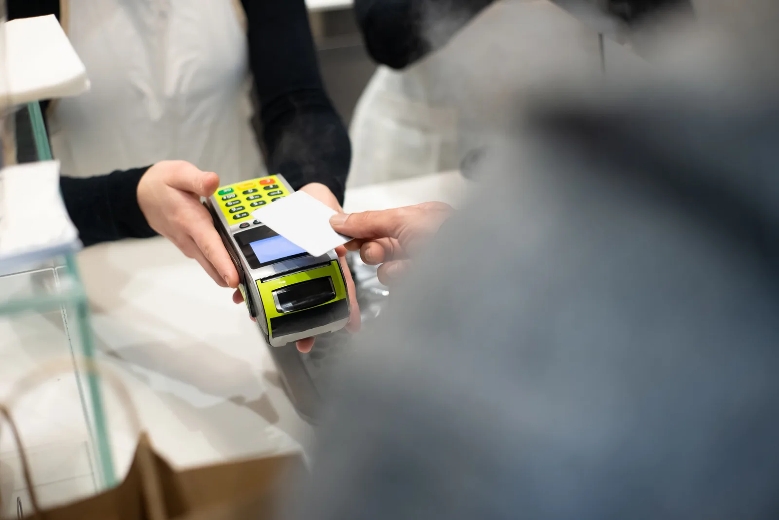 A shop assistant holds out a card payment terminal while a customer taps a bank card
