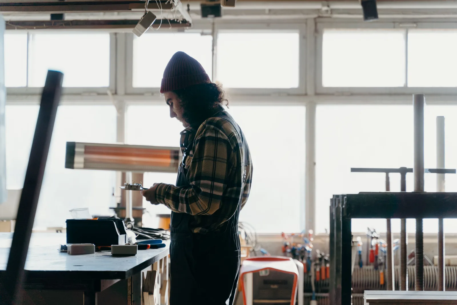 A tradesman working at a bench in a bright workshop, with hand tools and stock racked along the wall behind him.
