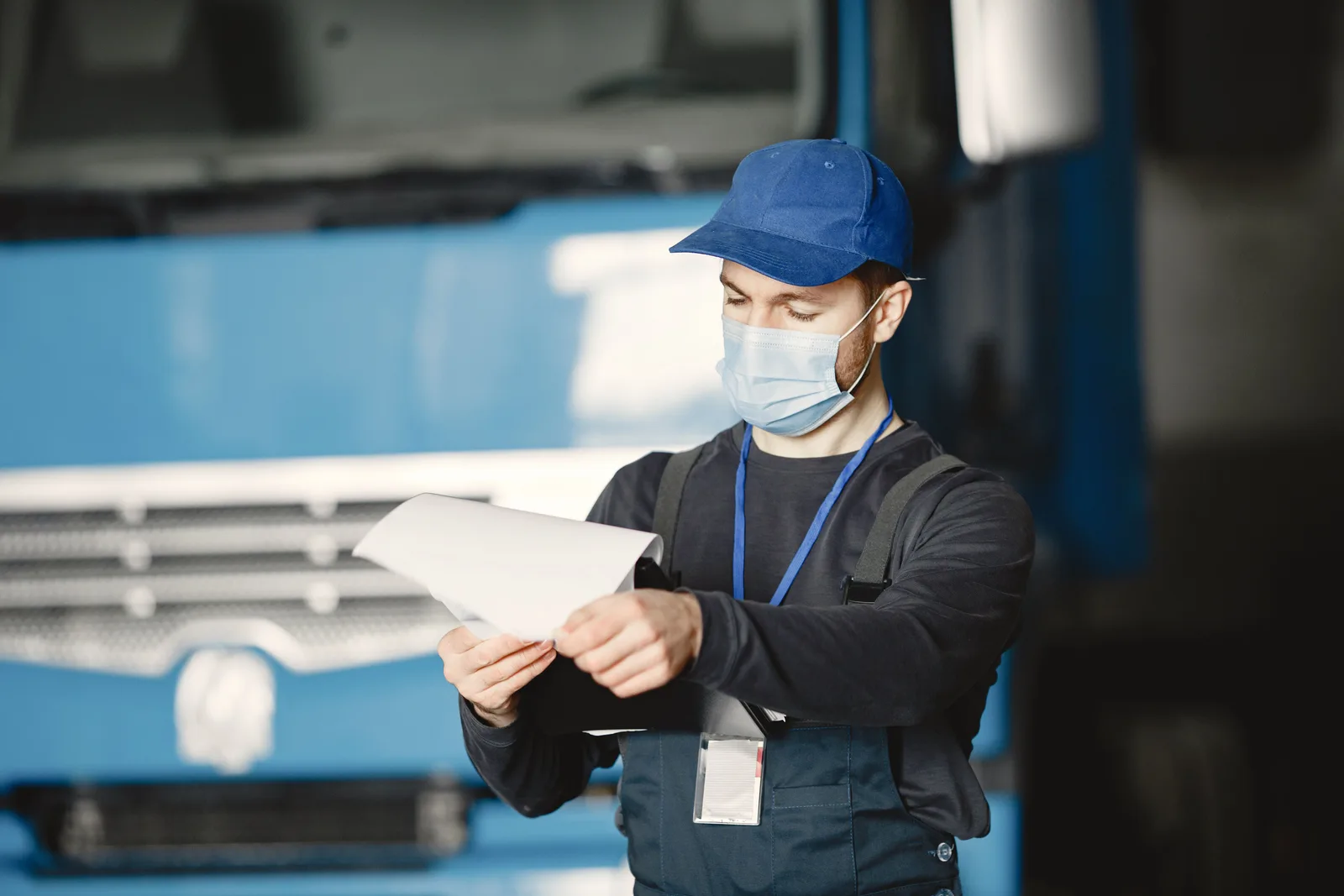 A mechanic in work clothes reading through a printed document in front of a truck inside a repair shop