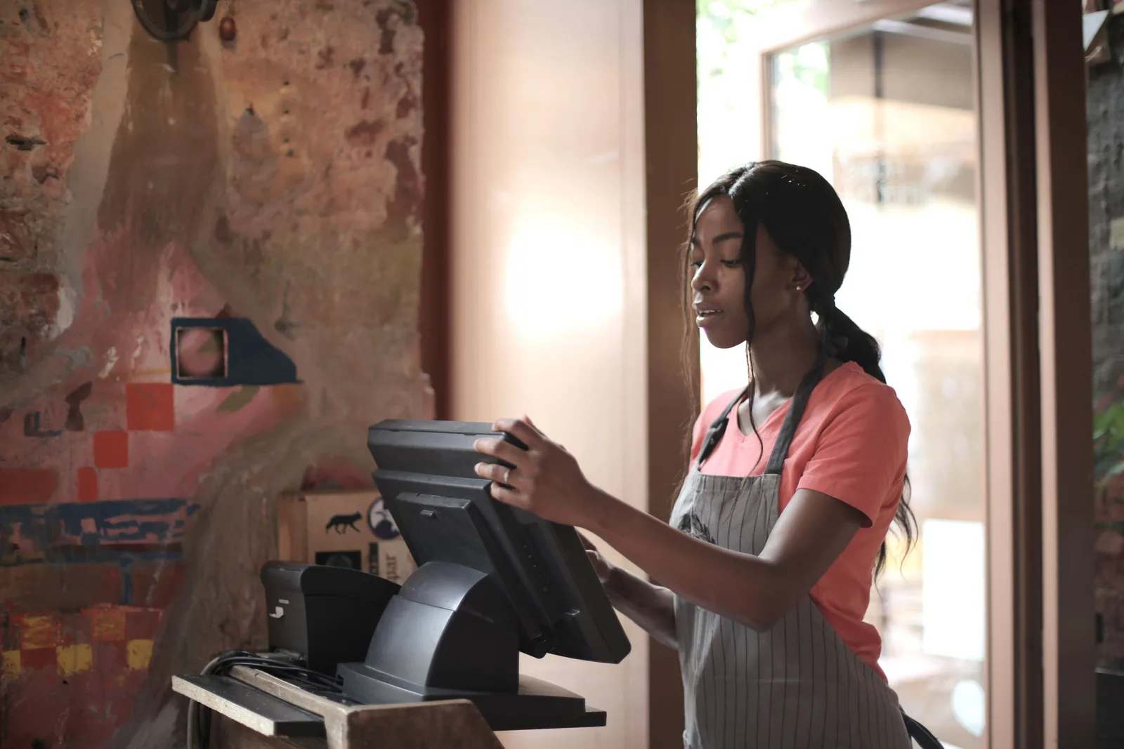 A shop worker in an apron ringing up a sale on the point of sale terminal at the counter of a small store.