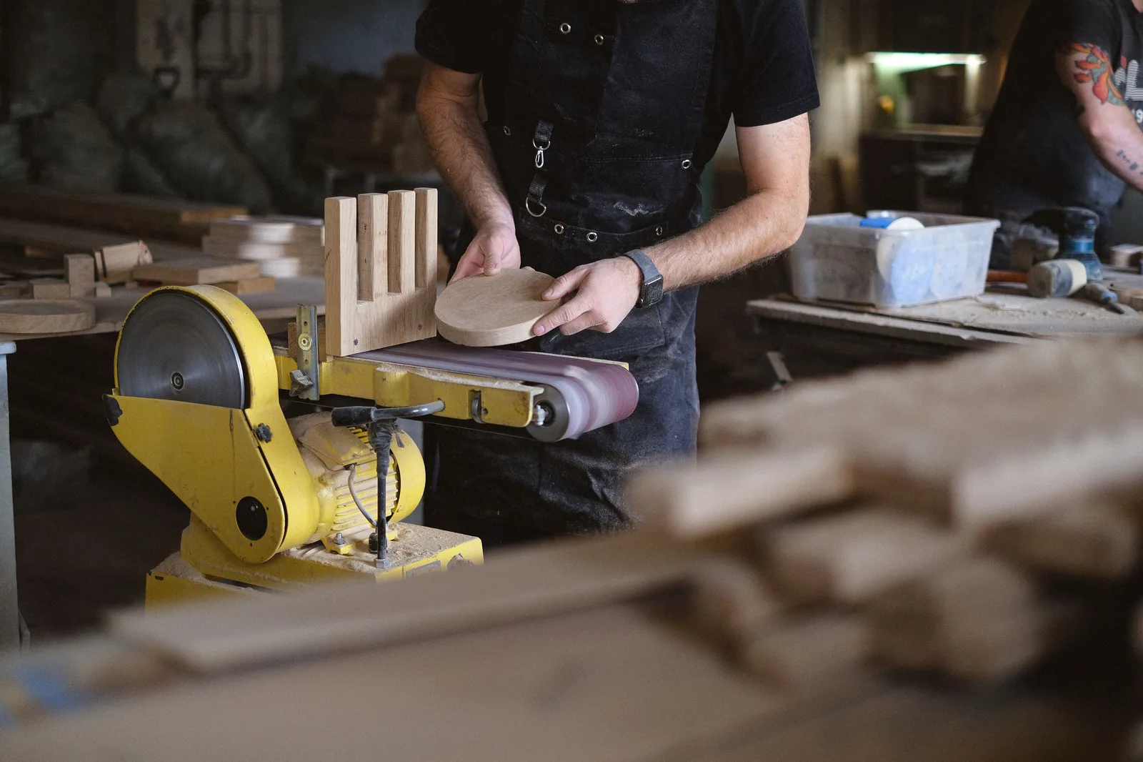 A woodworker shaping a piece of timber on a disc sander in a workshop