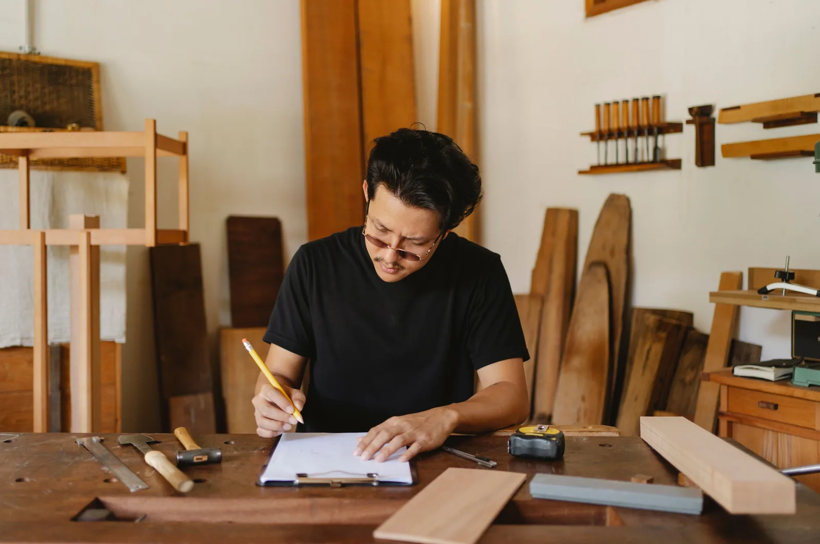 A craftsman writing notes on a clipboard at a workbench