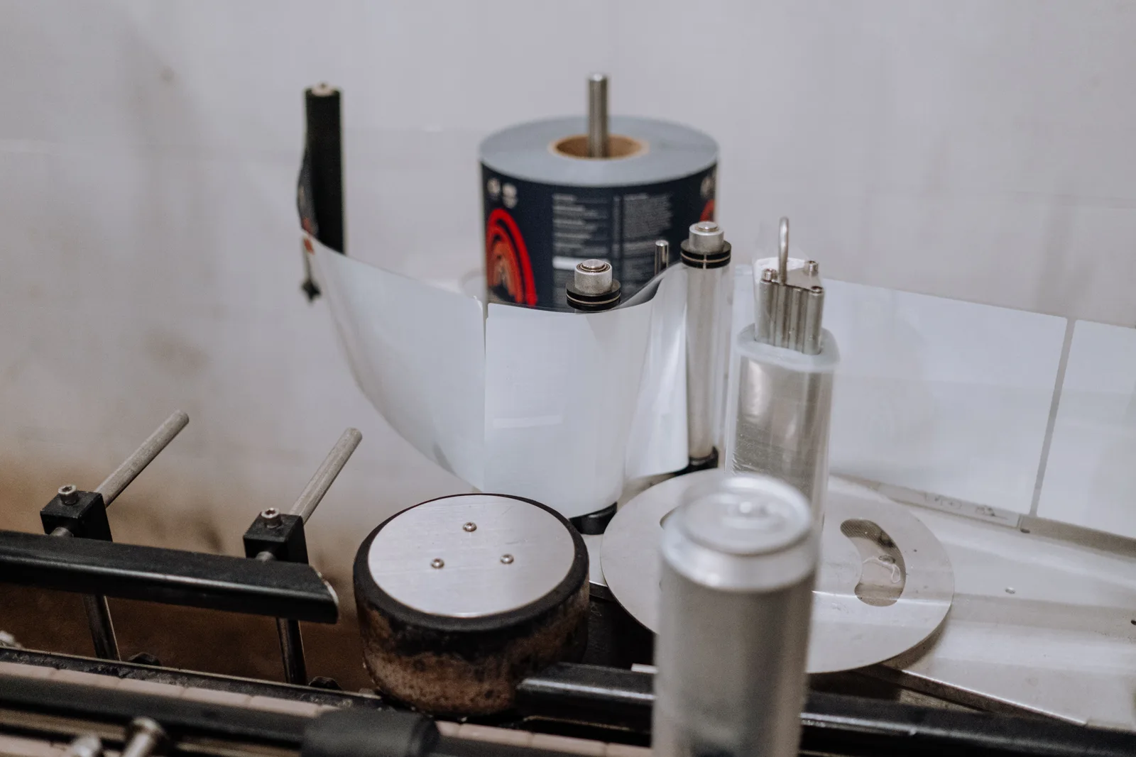 A roll of printed labels feeding through a bench labelling machine as an aluminium can passes along the applicator.