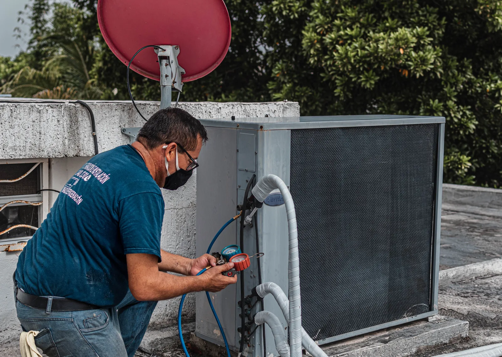 HVAC technician connecting refrigerant gauges to a rooftop packaged air conditioning unit beside its filter panel