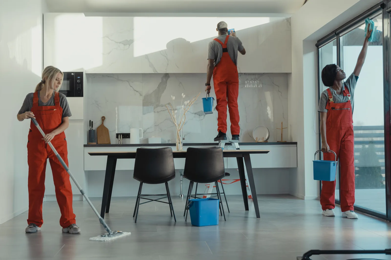 Three cleaners in red overalls mopping the floor and wiping the glass wall of an open plan interior.