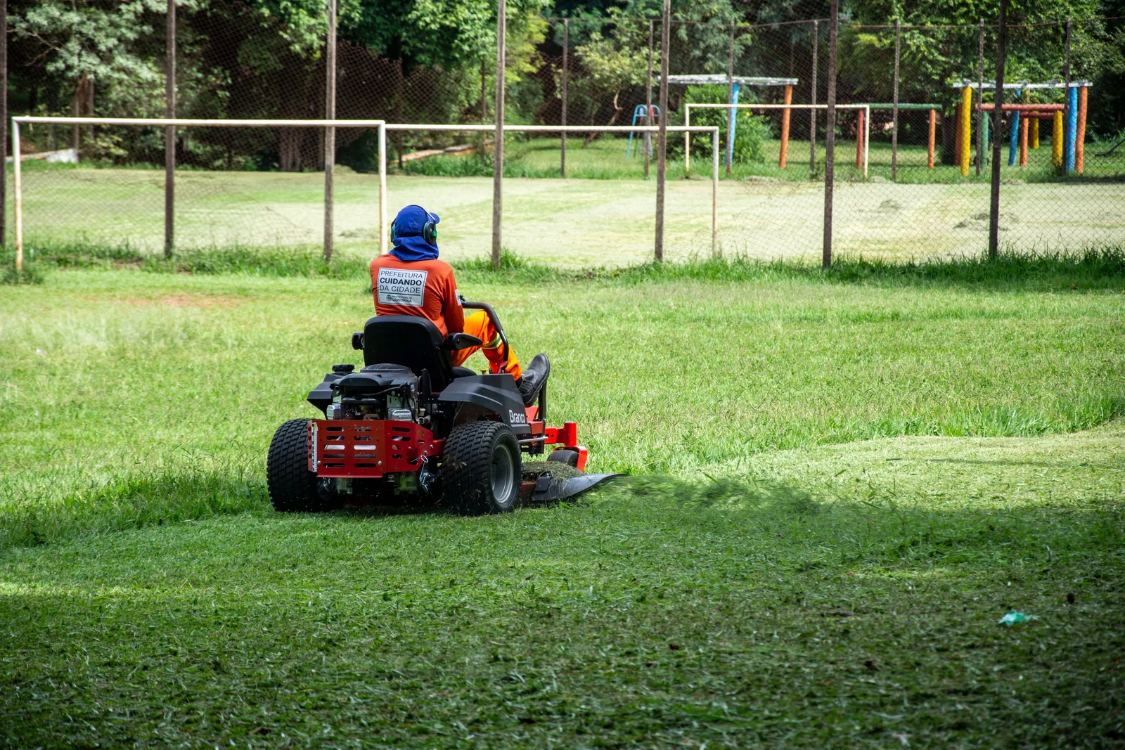Worker in high visibility clothing cutting a large grass area on a riding mower