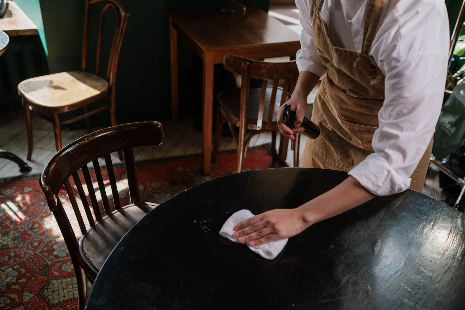 Server in an apron wiping down a round table between covers in a small dining room