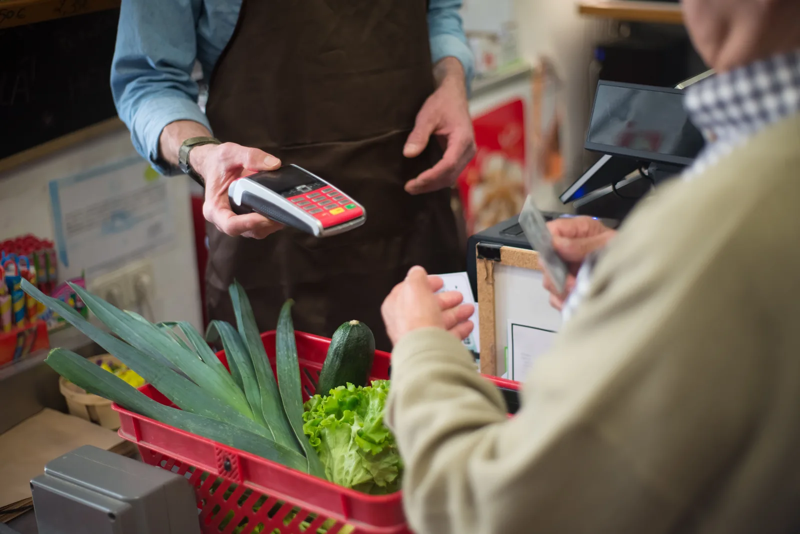 A grocer holding out a card payment terminal to a customer buying vegetables