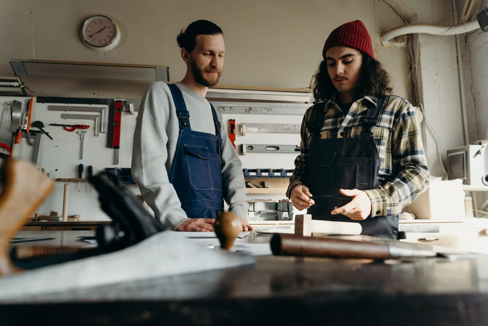 Two joiners stand at a bench in a woodworking shop looking over a piece of work.