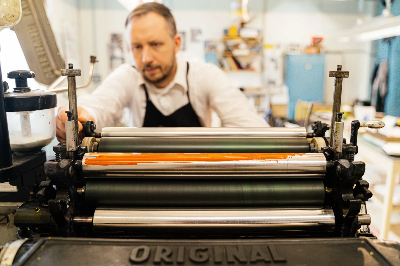 A printer reaches across the inked rollers of a letterpress in a print workshop.