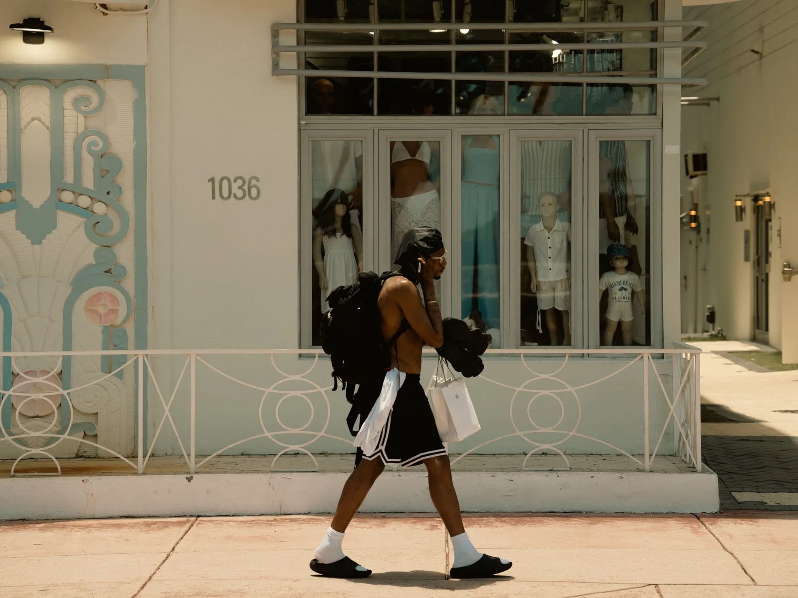 A man carrying shopping bags walks past an art deco boutique on a Miami Beach street