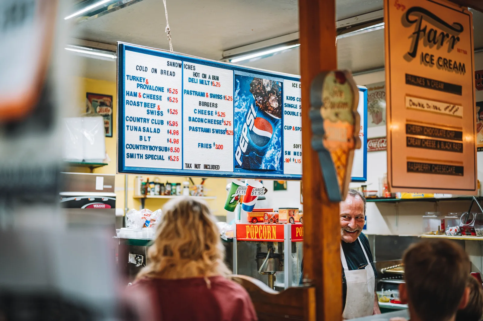 Customers ordering at a deli counter under a printed menu board