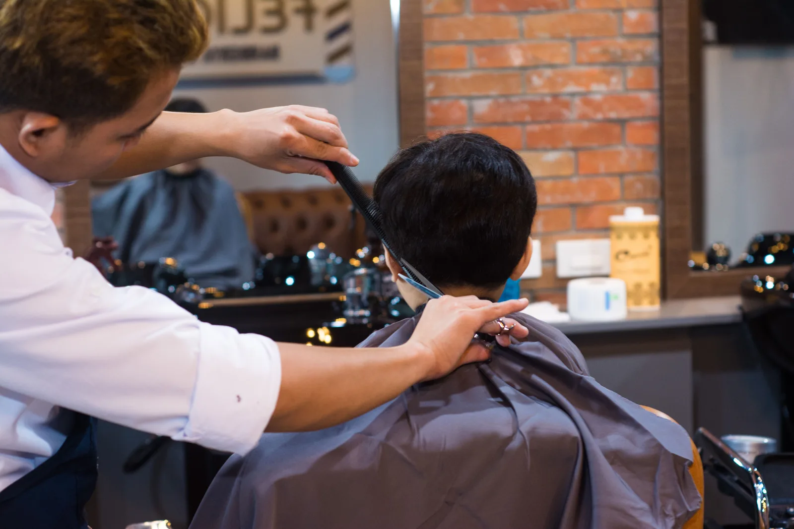 A barber combs and cuts a seated client’s hair in a barbershop.