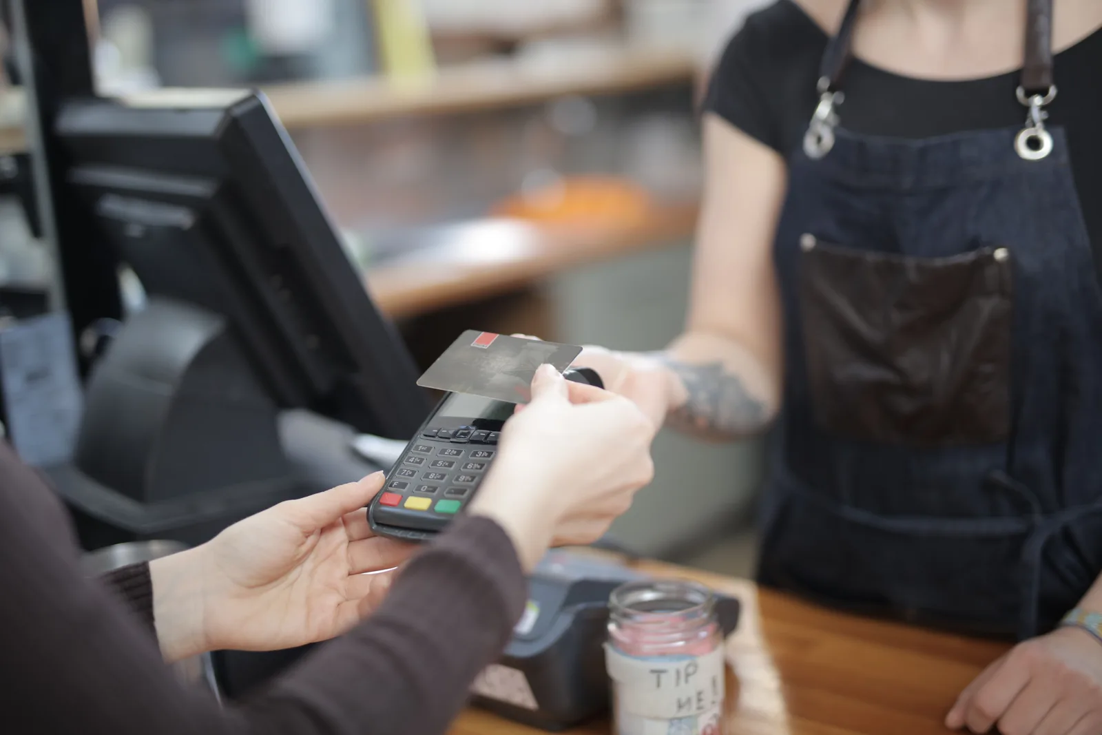 A close view of a customer handing a card to a member of staff across a shop counter beside the register
