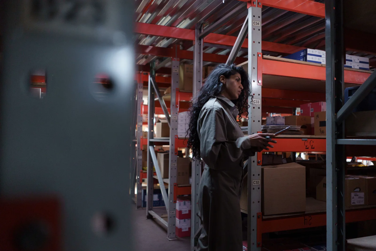 A worker holding a tablet checks stock along a racked stockroom aisle.
