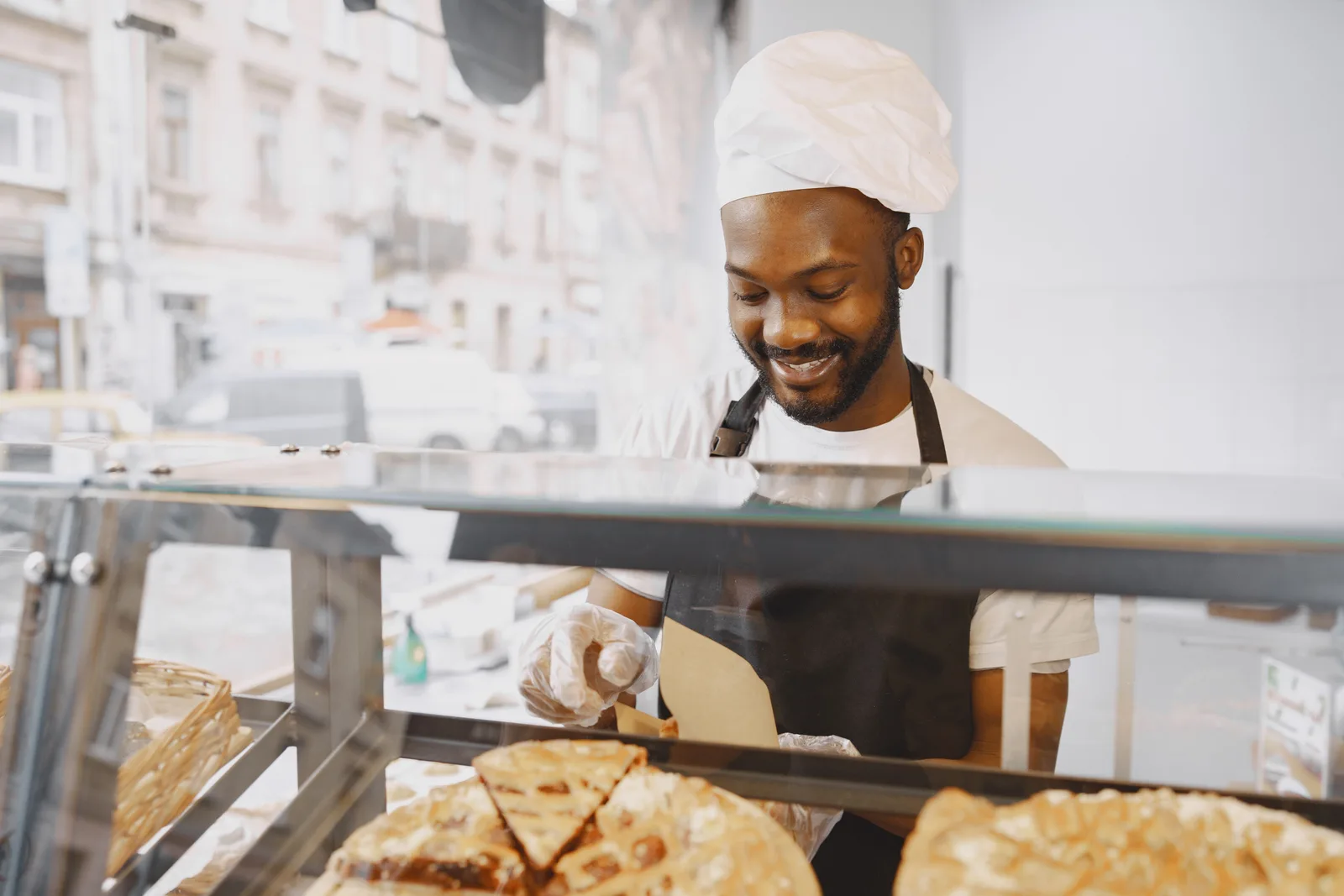 A baker in an apron serving pastries from a bakery display case