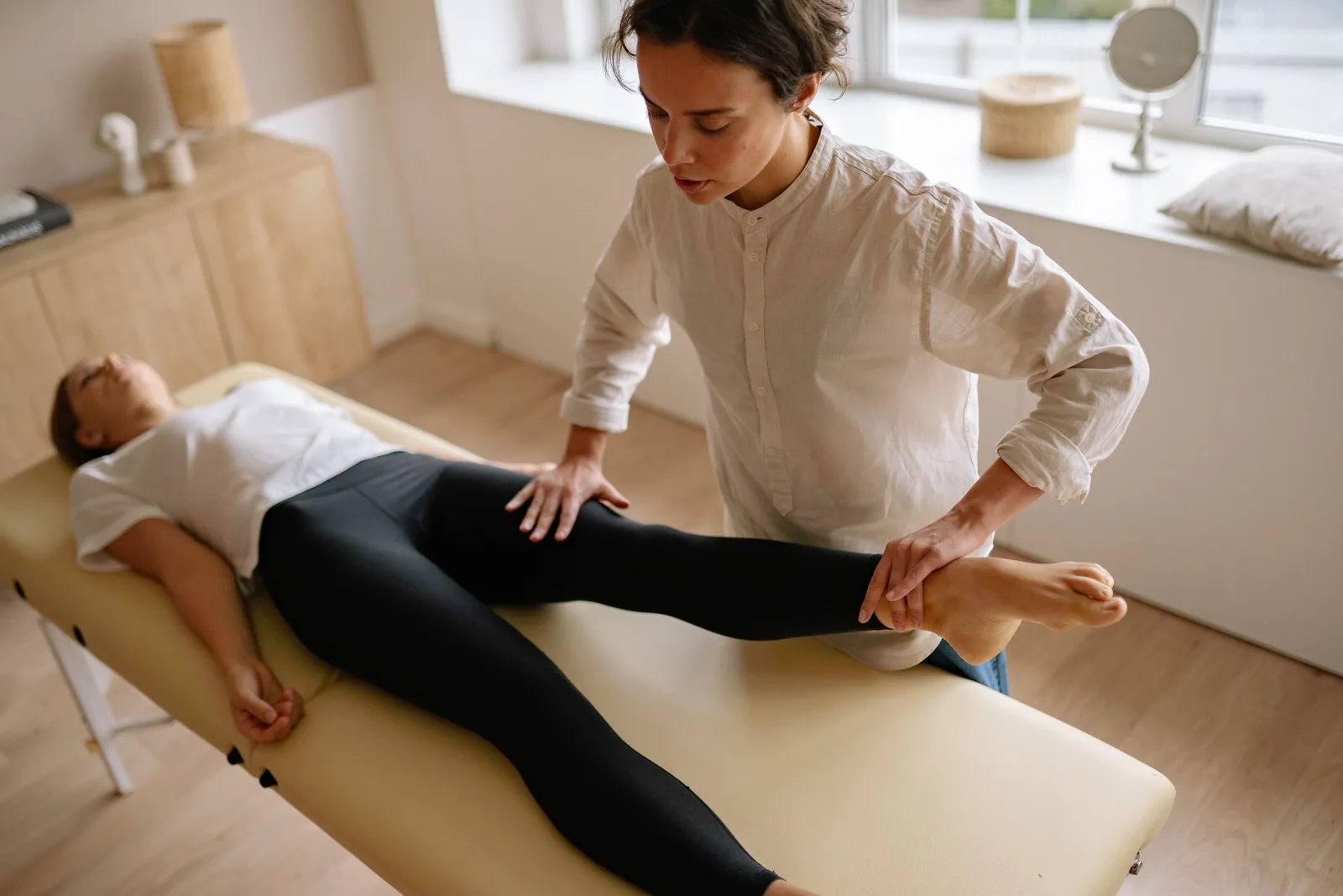 A physiotherapist supporting a patient's leg during a session on a treatment table