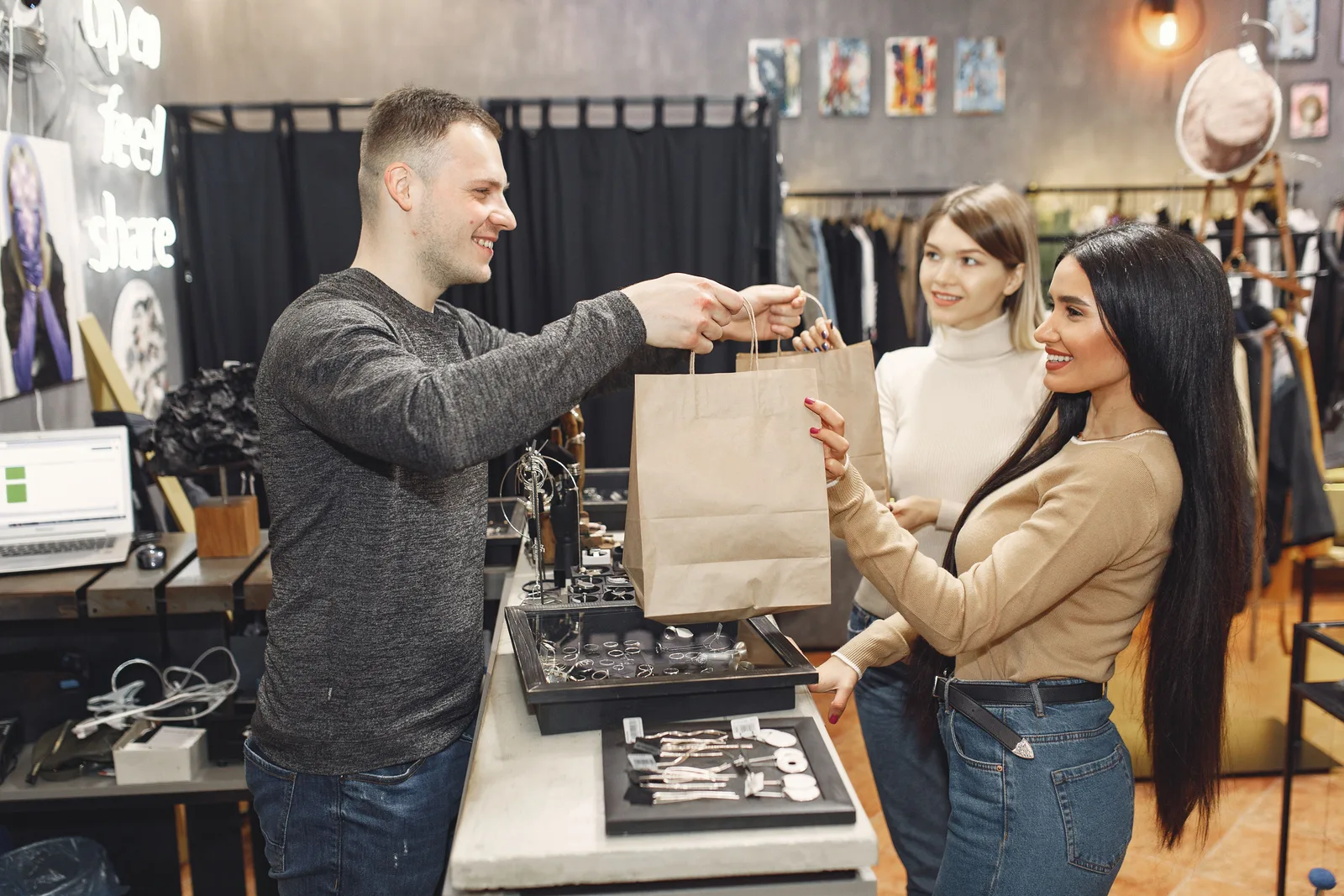 Shop assistant passing paper bags across a counter to two customers in a boutique