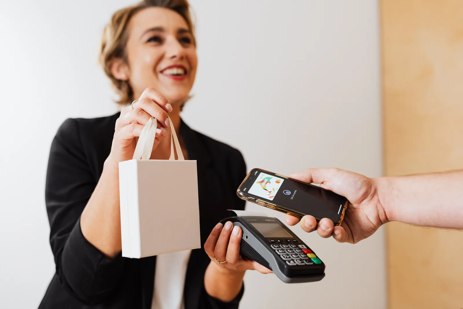 Shop assistant holding a card terminal while a customer pays by tapping a phone