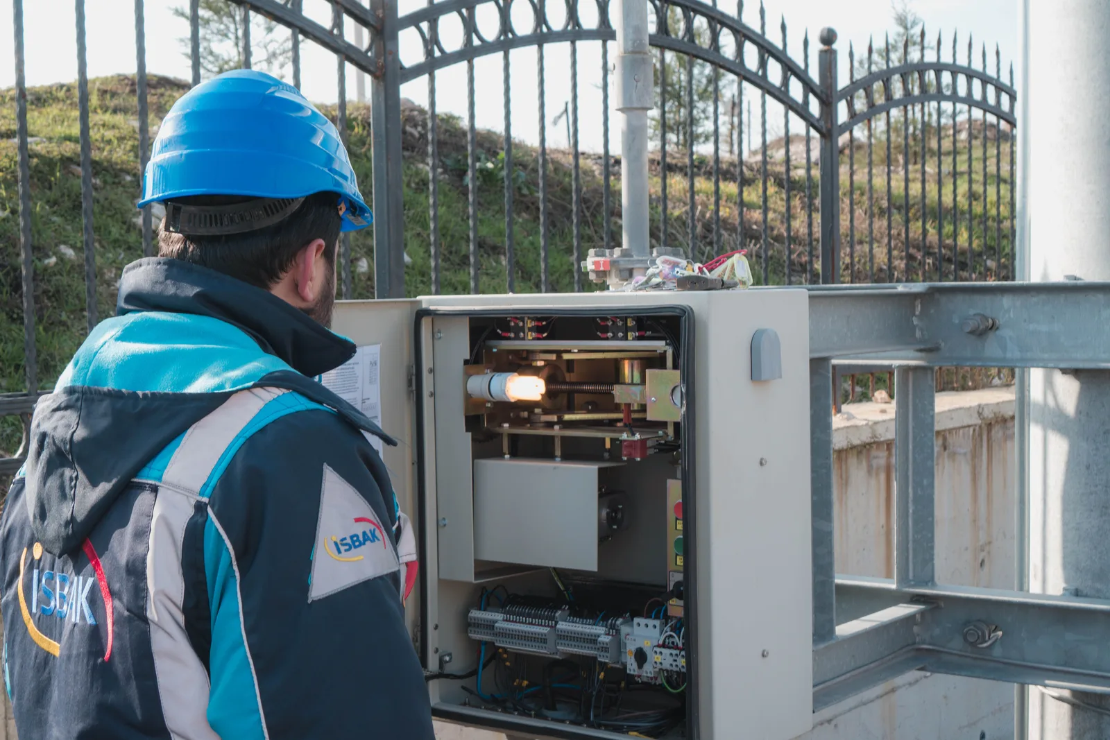An electrician in a hard hat working inside an open outdoor electrical cabinet