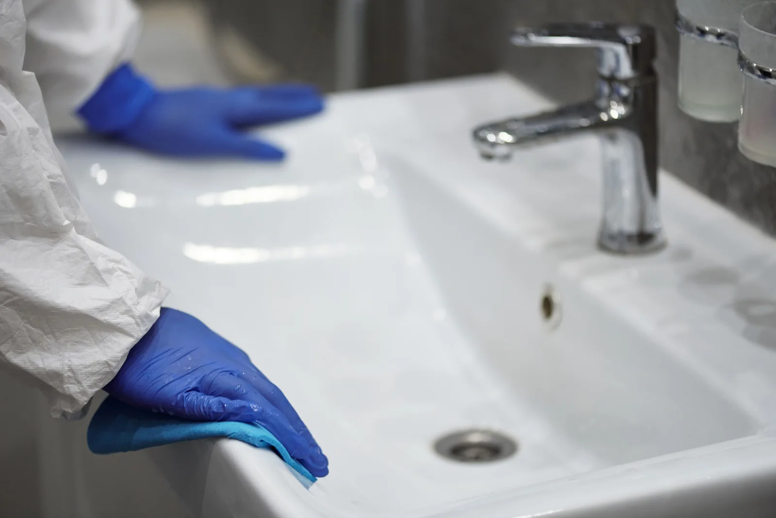A gloved cleaner scrubbing a washbasin during a routine restroom clean.
