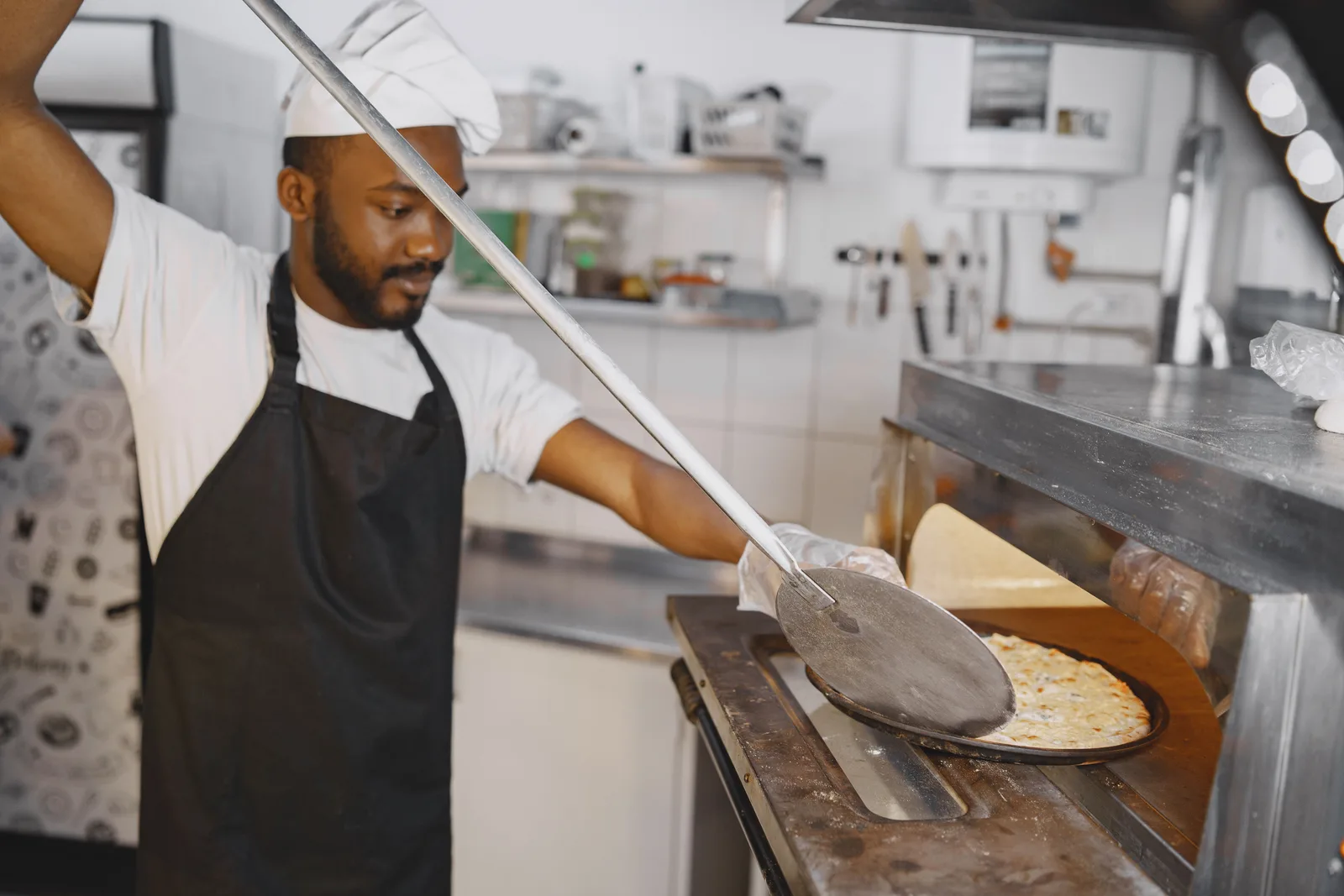 Cook sliding a pizza into a deck oven with a long metal peel