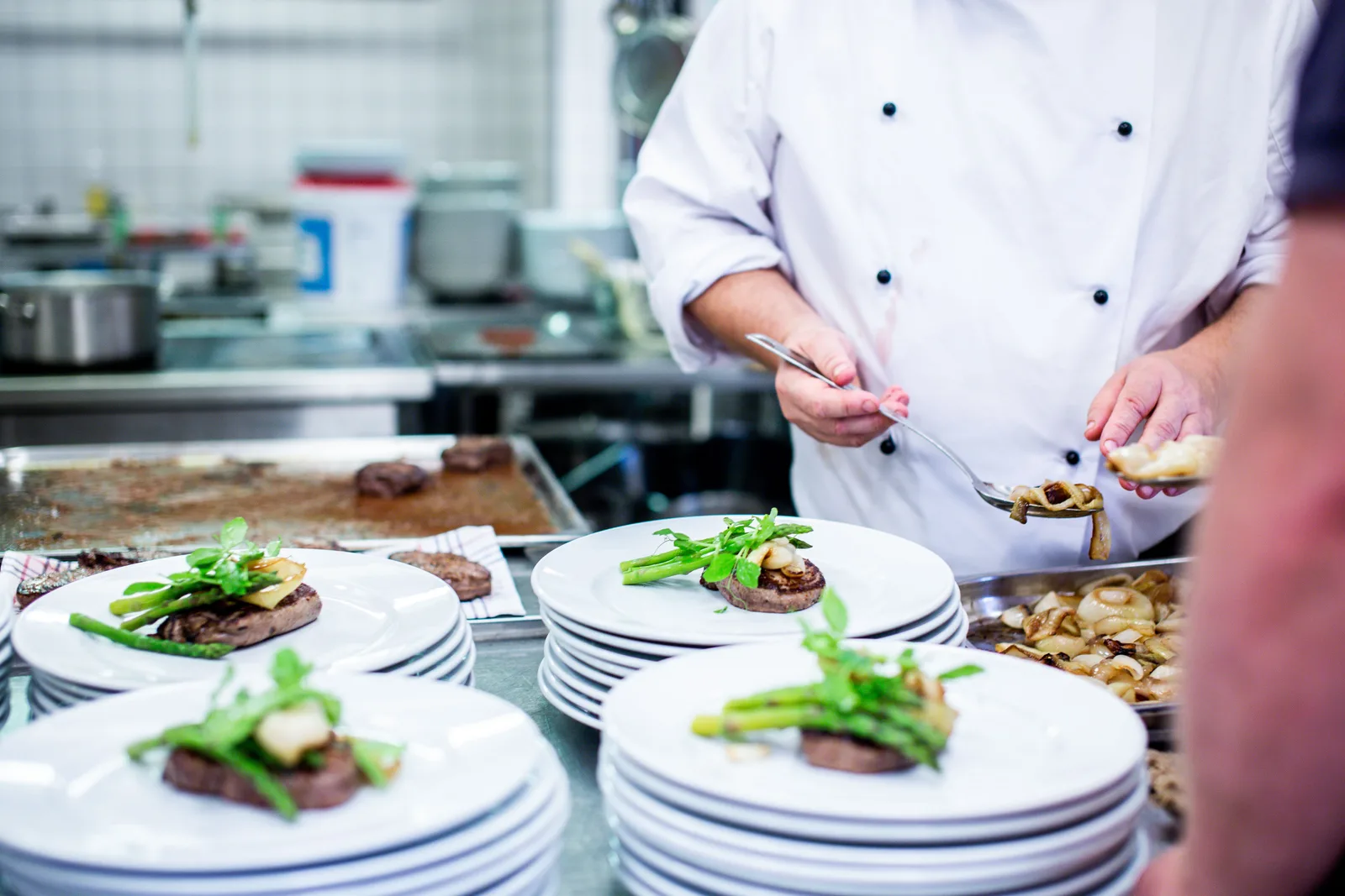 A chef in whites plating food onto a row of prepared plates on a restaurant kitchen pass