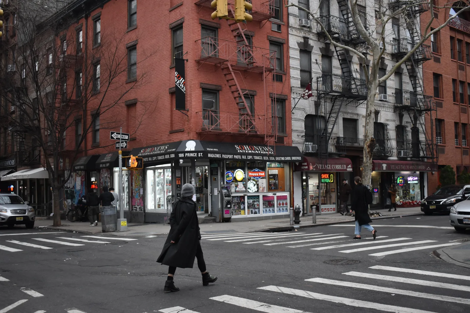Pedestrian crossing an intersection lined with ground floor shops and apartment buildings in Brooklyn