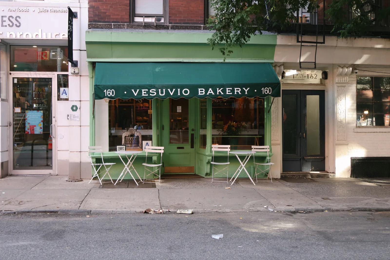 Corner bakery with a green painted front and outdoor seating on a New York City street