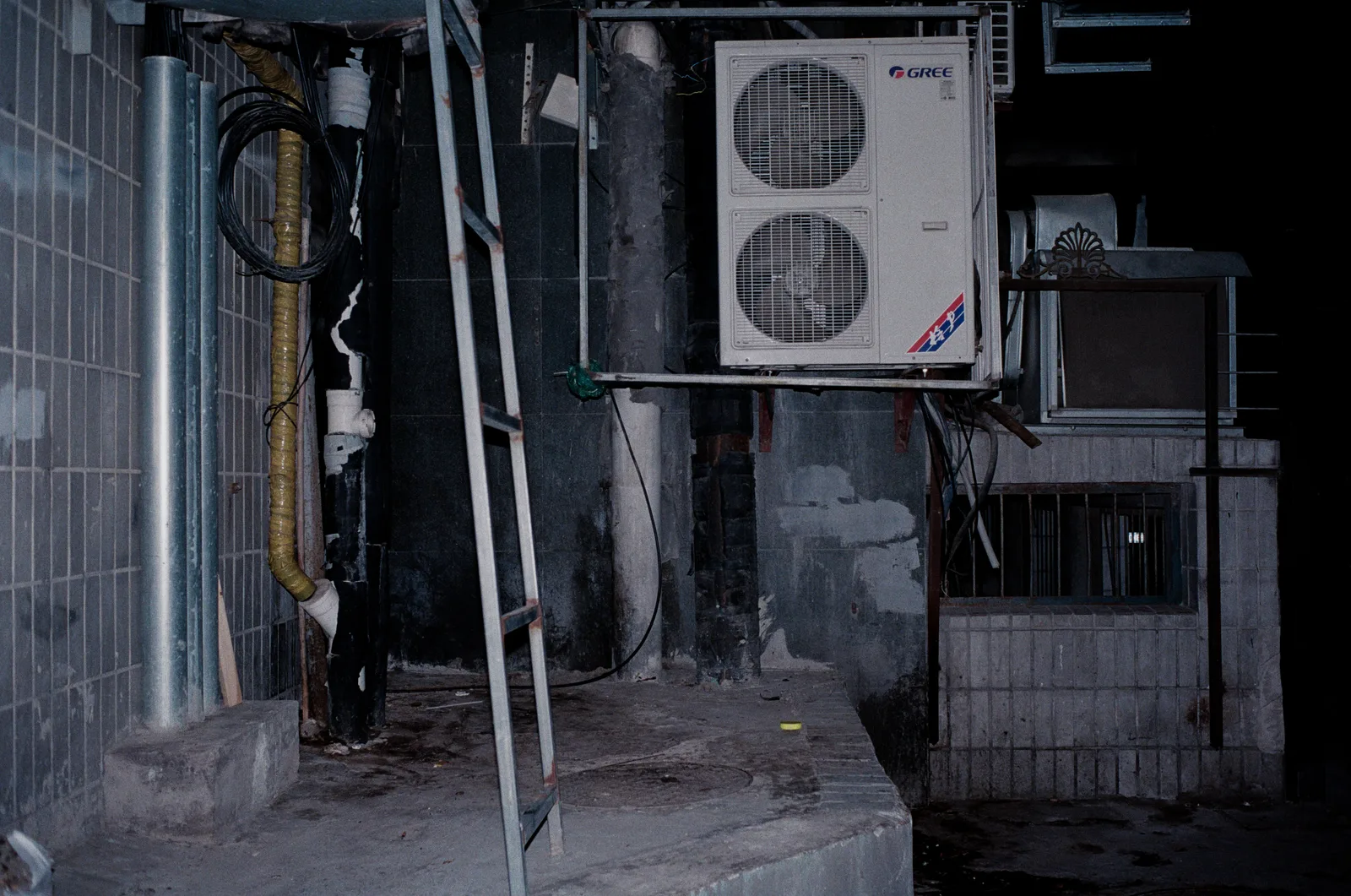 Air conditioning condensers and refrigerant pipework mounted on a building wall beside a fixed ladder