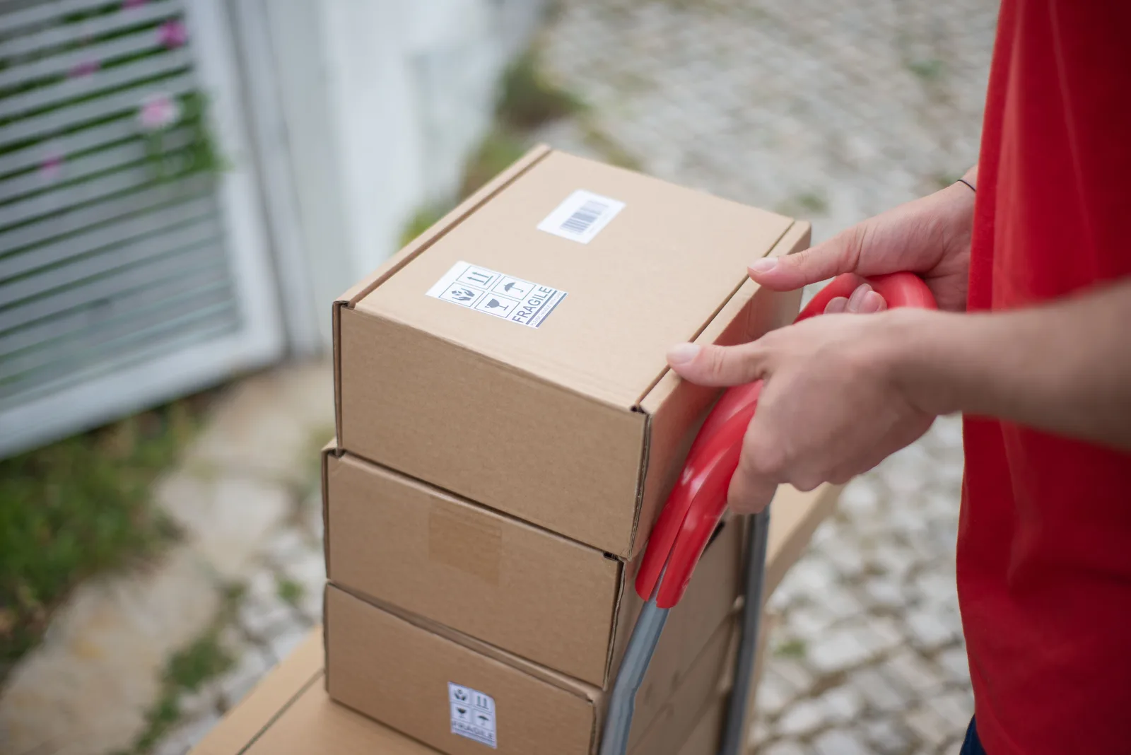 Worker pushing a hand trolley stacked with cardboard boxes outdoors