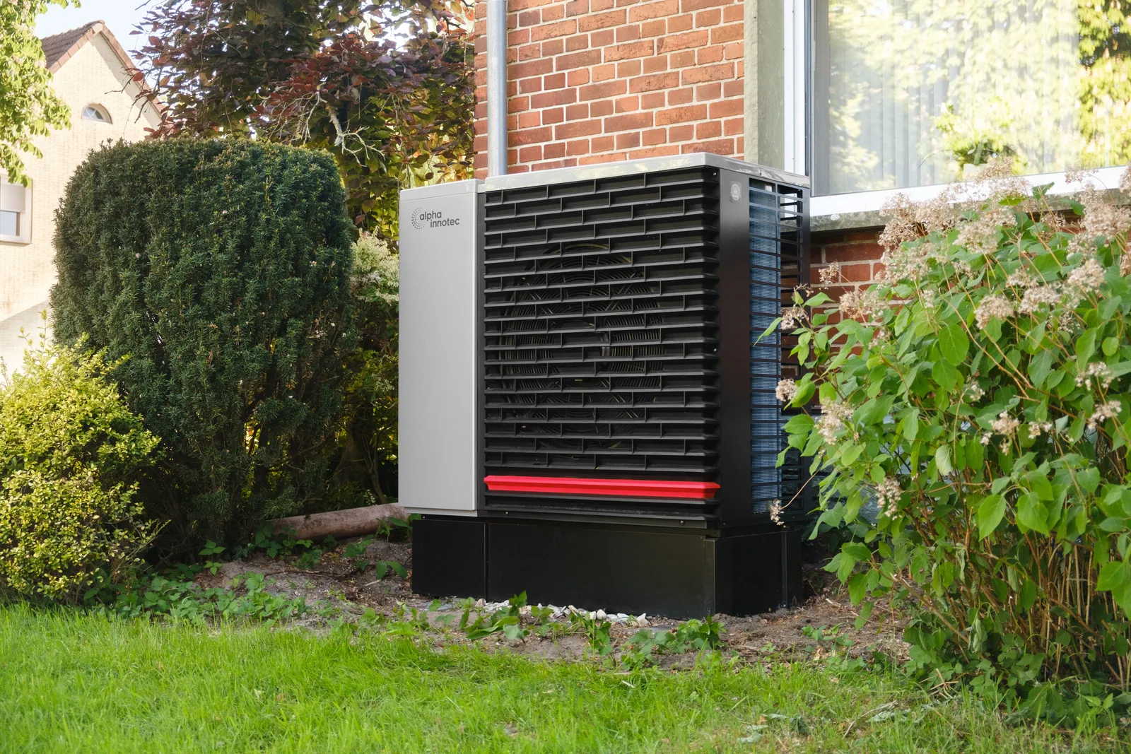An outdoor heat pump unit installed on a pad beside a house in a green garden