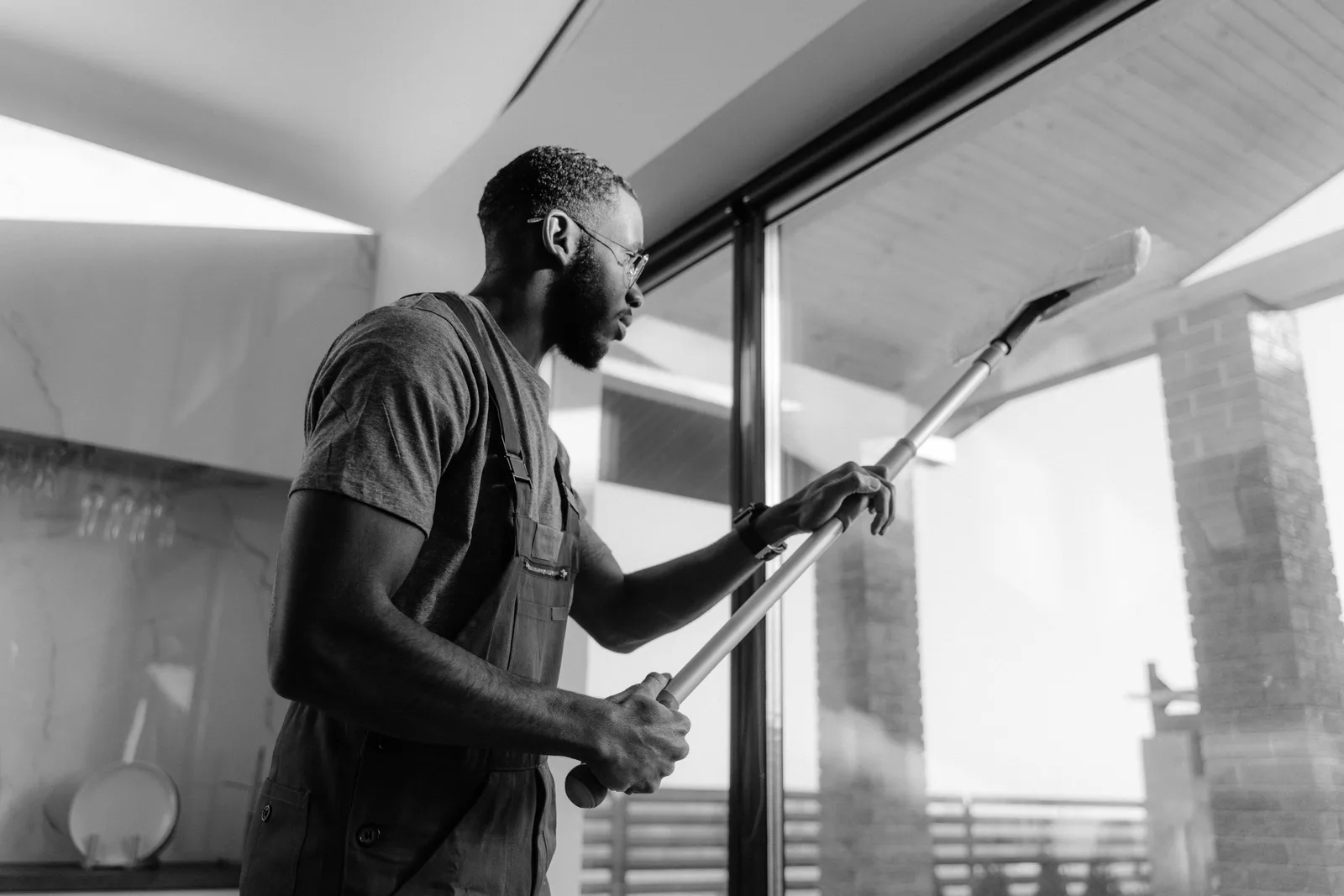 A cleaner in uniform wiping a floor to ceiling glass panel inside a modern office building.