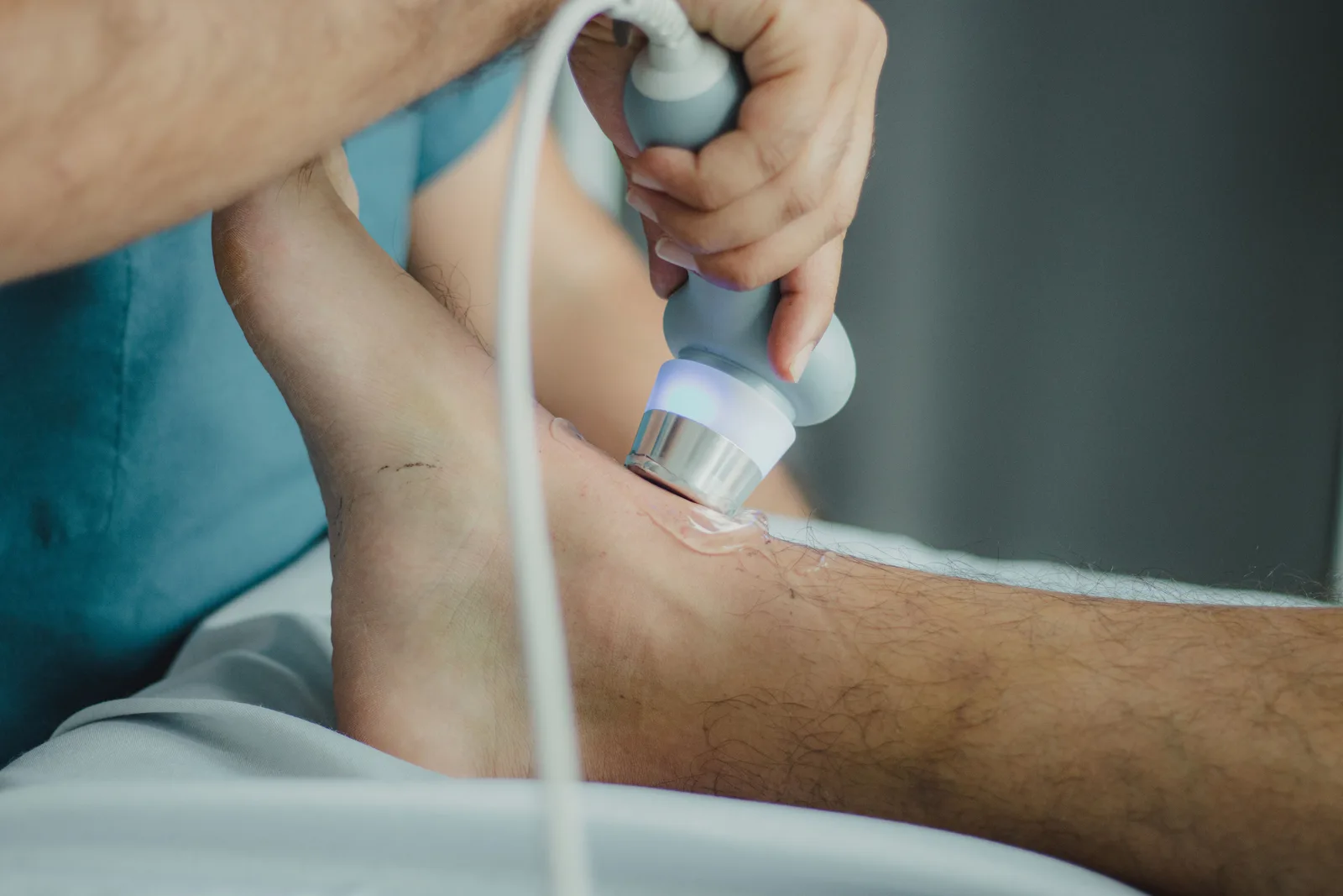 A physiotherapist treating a patient's lower leg with a hand-held ultrasound therapy head