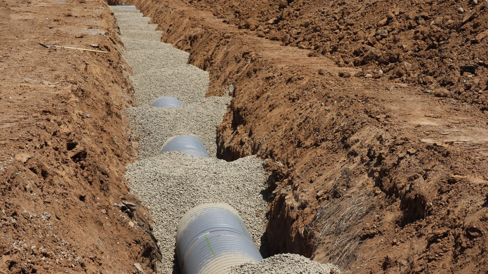 A newly laid pipe bedded in gravel along the bottom of an open trench at a construction site