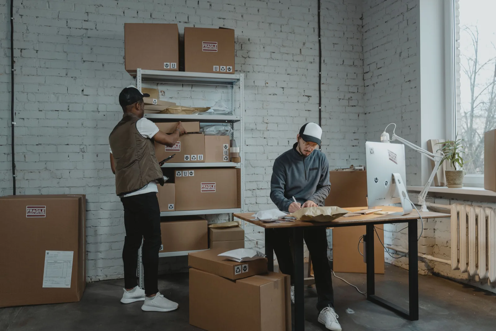 Two workers handling packages and organizing stock in a small warehouse