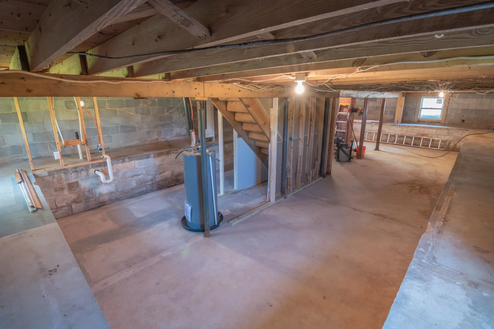 An unfinished basement with a water heater and exposed pipework running under the floor joists