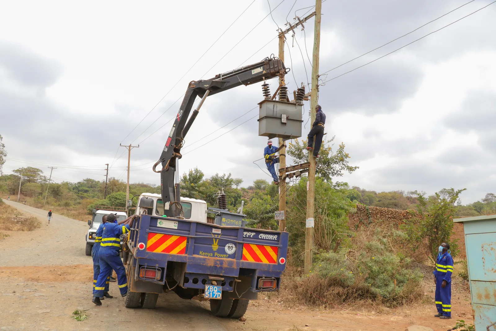 A line crew working from a boom truck to set equipment on a utility pole beside a rural road