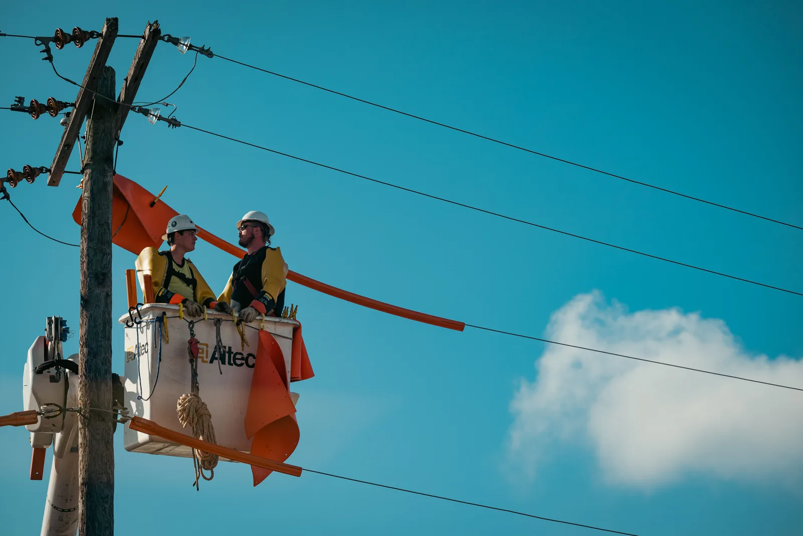 Dos electricistas trabajando desde una canastilla elevadora en la parte superior de un poste de servicio
