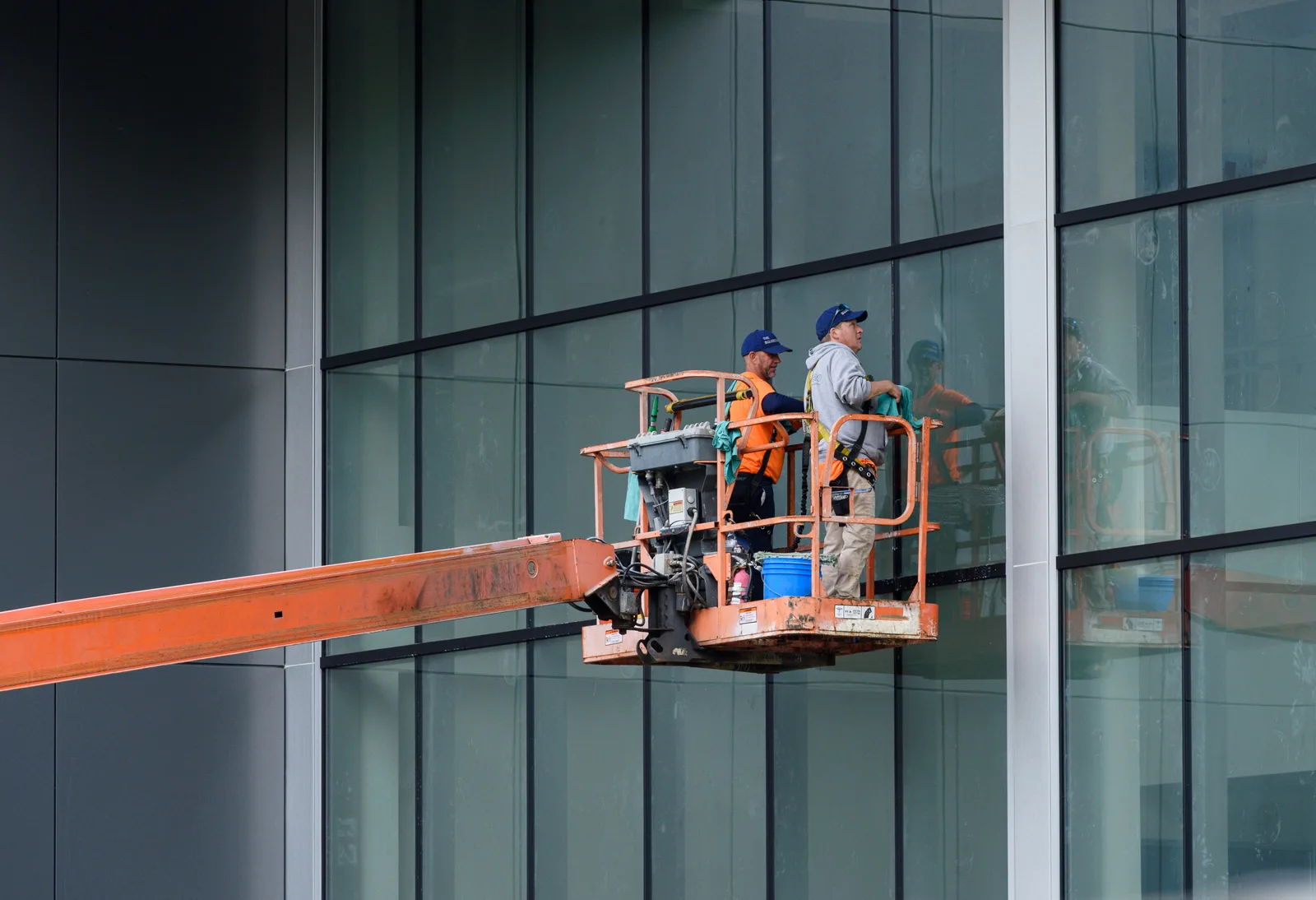 Two workers cleaning tall exterior windows from the basket of a boom lift.