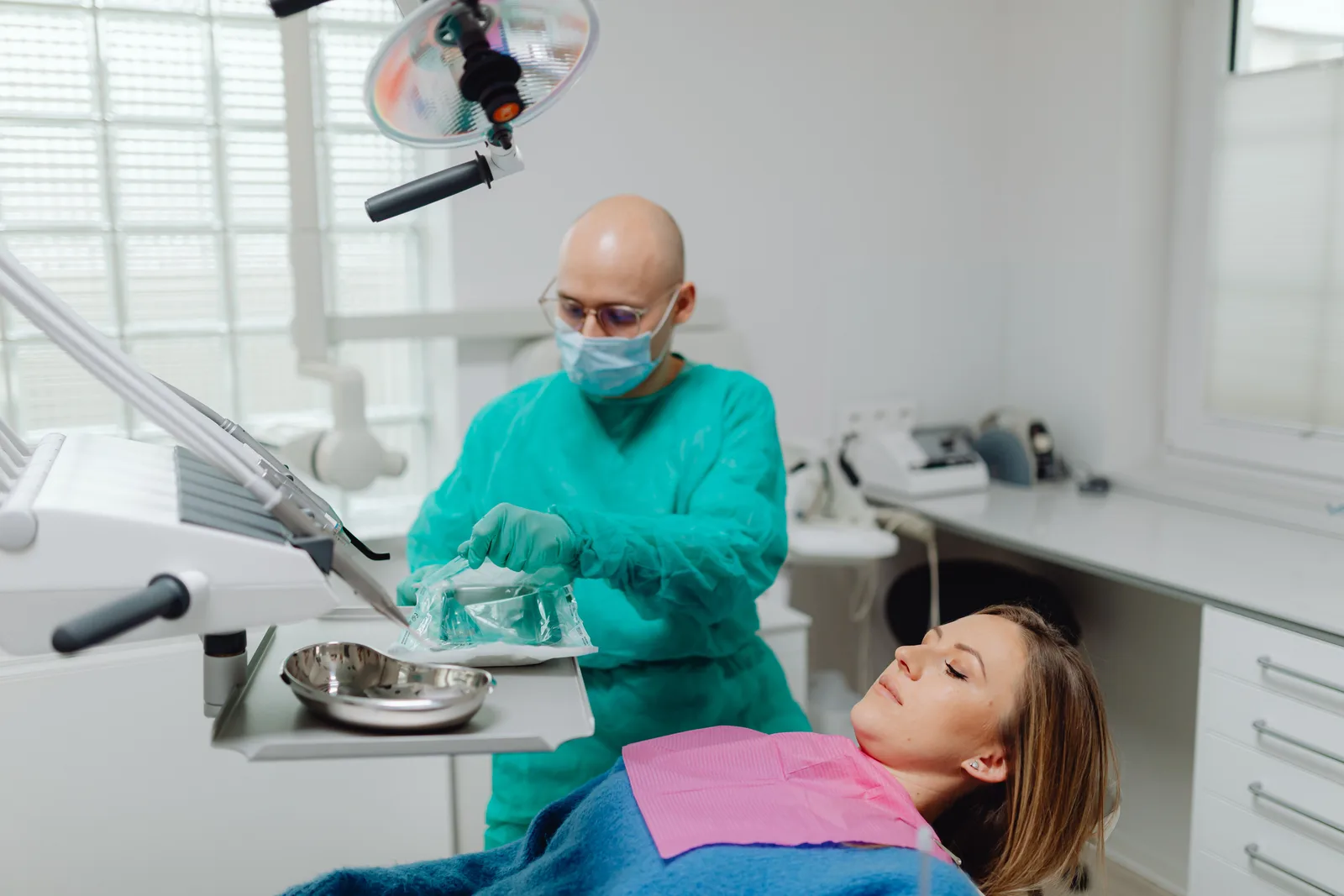 A gloved clinician opening a sealed pack of sterilised instruments beside a treatment chair